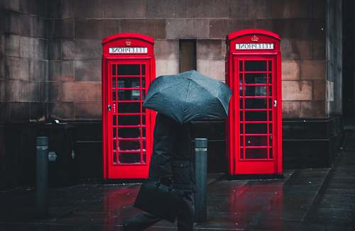 umbrella person under umbrella walking beside telephone booths manchester